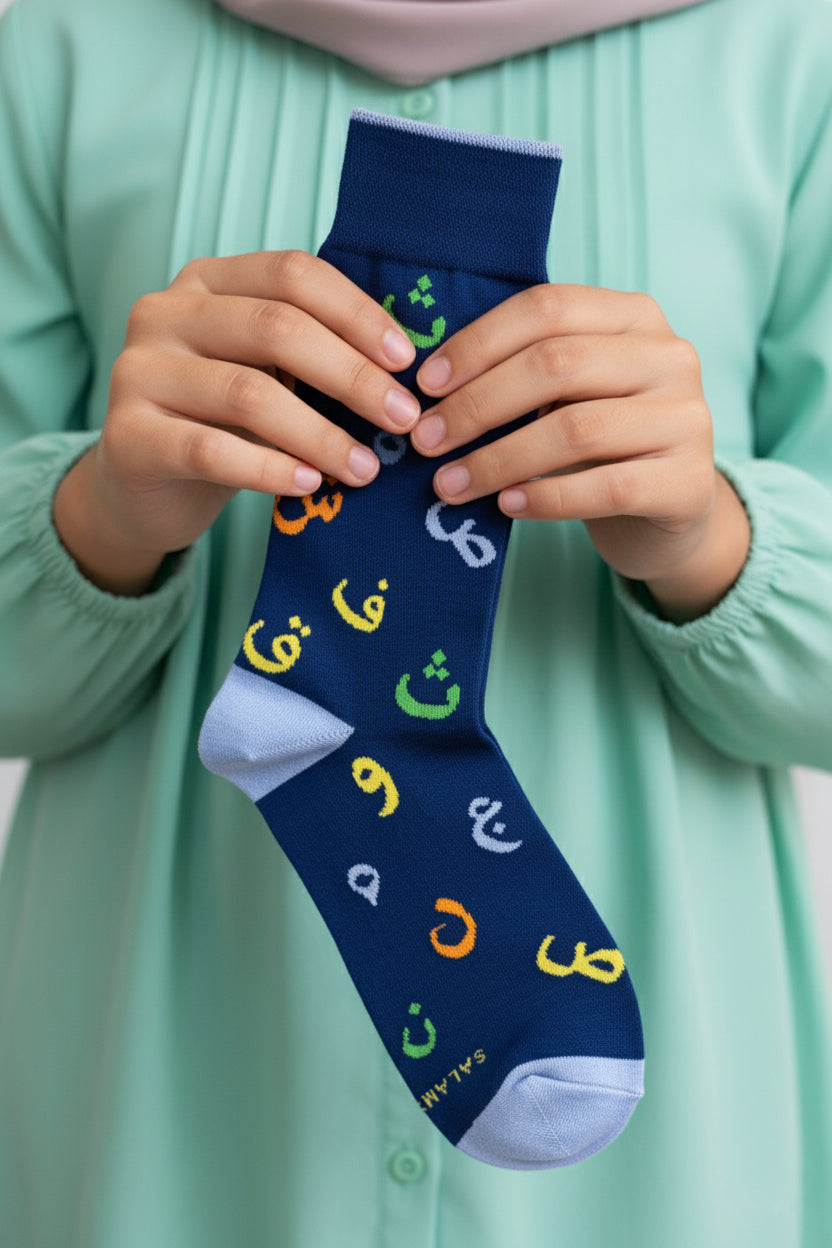 Person holding a navy sock with colorful Arabic letters against a light green background